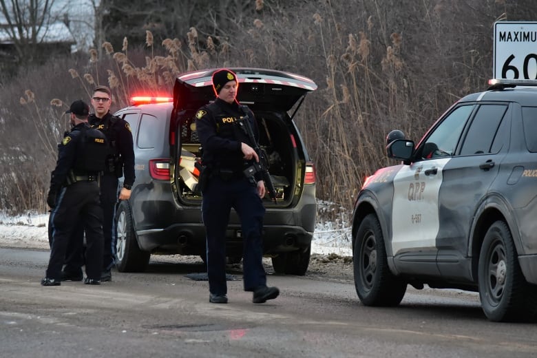 Police officers can be seen near their vehicles near the side of a road.