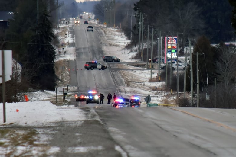 Police cars and officers can be seen in a rural outdoor road setting.