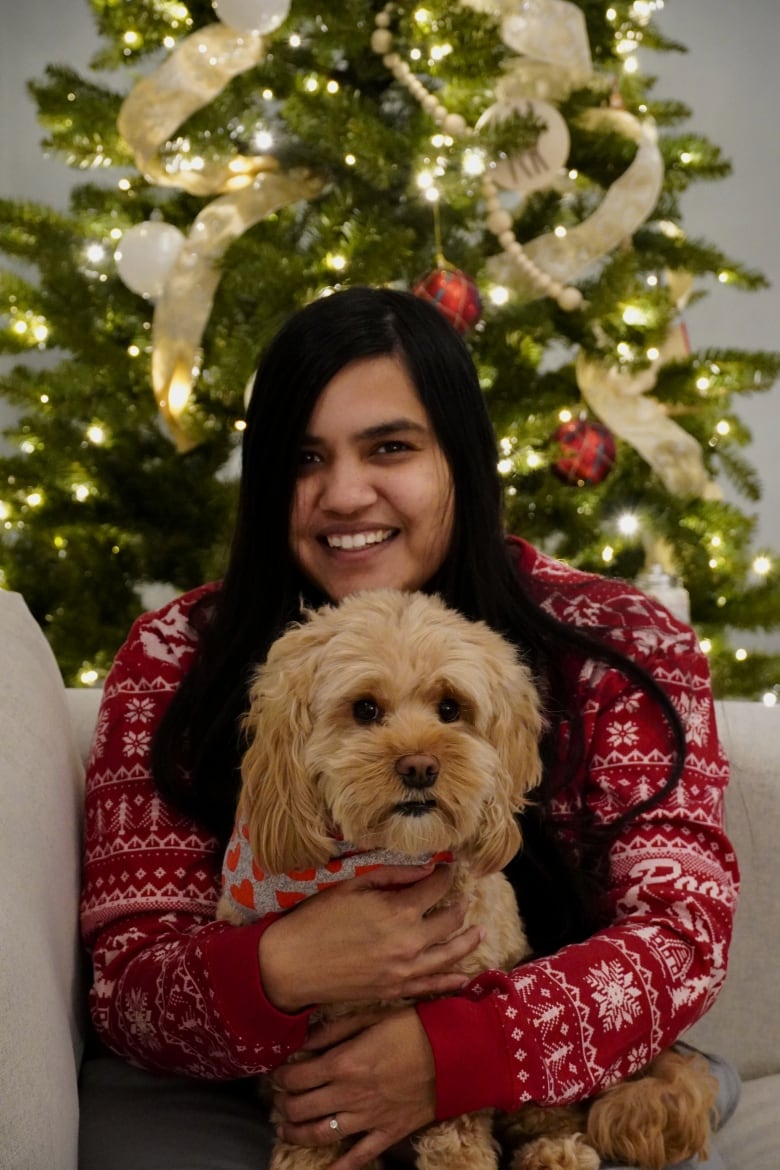 woman smiling in front of christmas tree with a dog on her lap