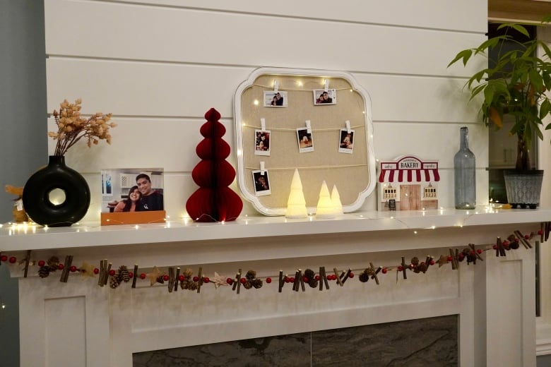 Une cheminée blanche est décorée de photos de famille, d'une guirlande, de lumières et d'autres décorations de Noël.