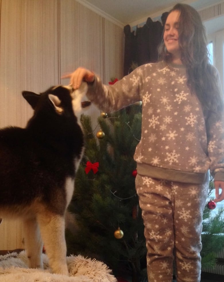 A woman plays with a dog in front of a Christmas tree. 