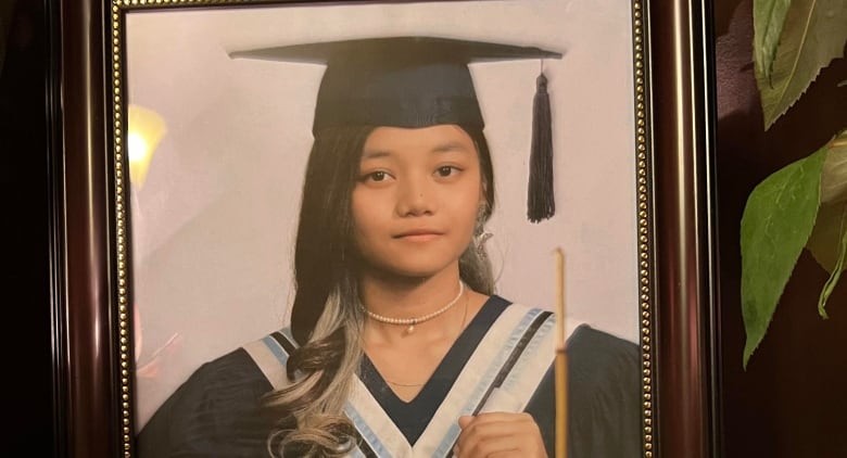 A teenager in a cap and gown sits for a portrait.