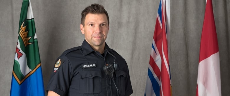 Constable Wade Tittemore stands between provincial and Canadian flags in a file photo for the Nelson Police Department. 
