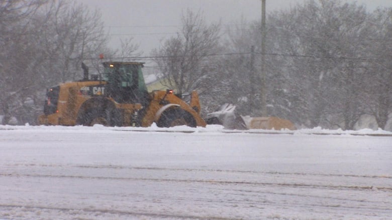 A snow plow clears the parking lot of a shopping mall.