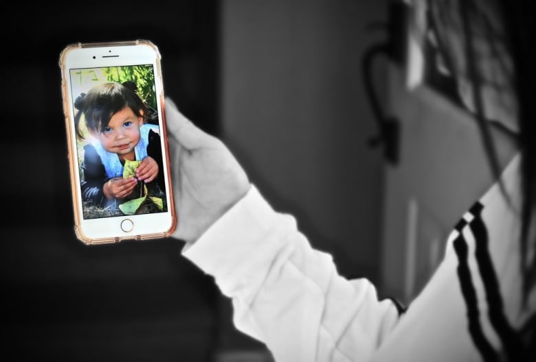 A photograph of a little girl is seen on a cellphone held by an adult.
