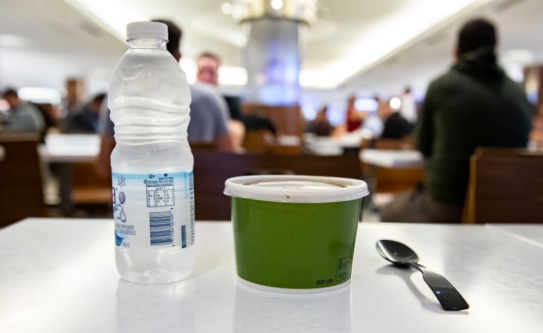 A plastic water bottle, green container and spoon rest on a table.