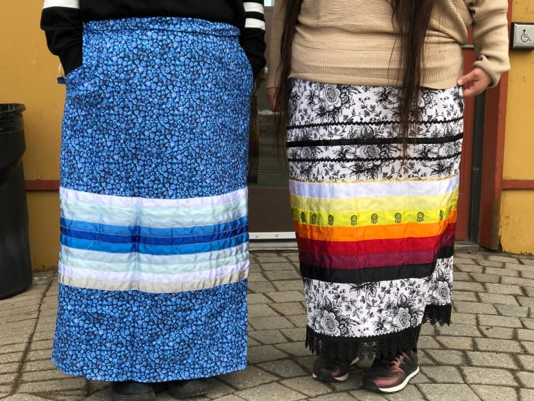 Two ribbon skirts: one is blue and one is black and white with colourful ribbons sewed on.