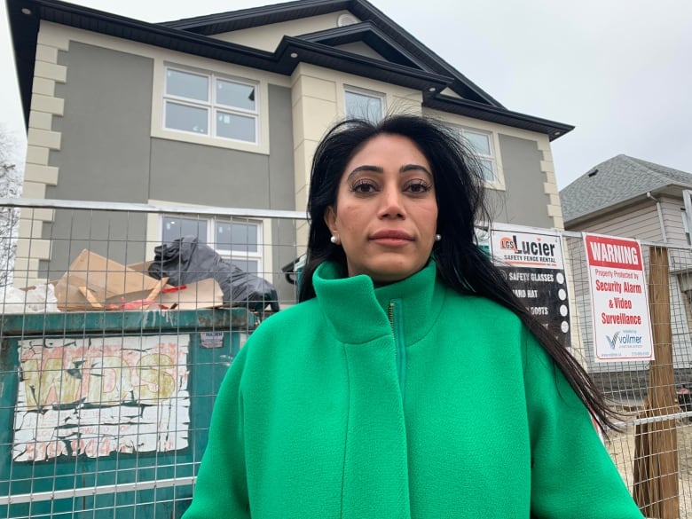 Woman in a green coat stands in front of an apartment building built in Windsor.