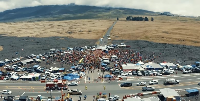 An aerial shot showing protesters and cars blocking the road to a mountain.