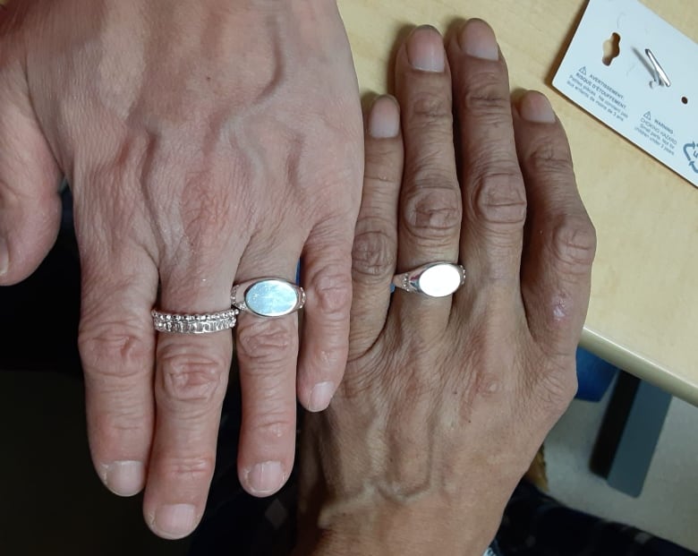 A close up of two hands wearing matching silver wedding rings.