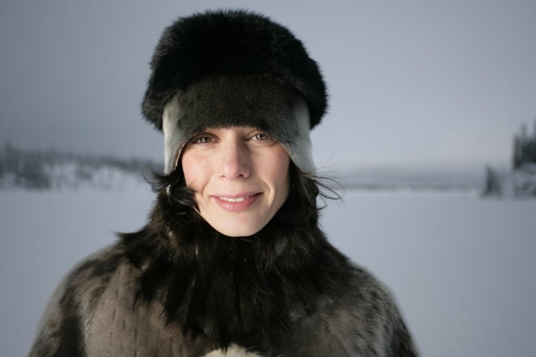 A woman, standing outside in the winter, wears a black and grey fur hat and coat. 