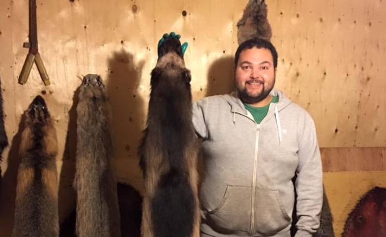 A man stands in a room holding up animal pelts