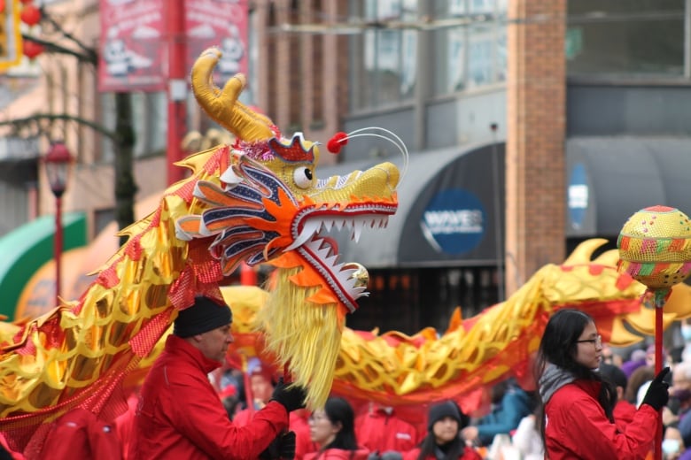 A group of people hold up a large red and yellow dragon at a Lunar New Year parade.