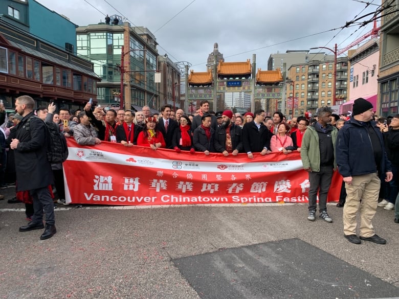 A collection of people pose with a red flag that reads 'Vancouver Chinatown Spring Festival' at the head of a parade.