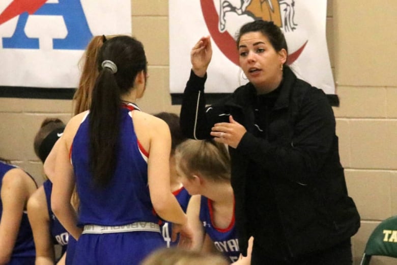 A woman coaching basketball gestures and speaks to a younger woman who is playing basketball. 