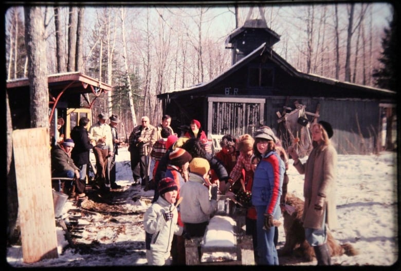 Snowy spring scene with people in front of a small sugar shack.