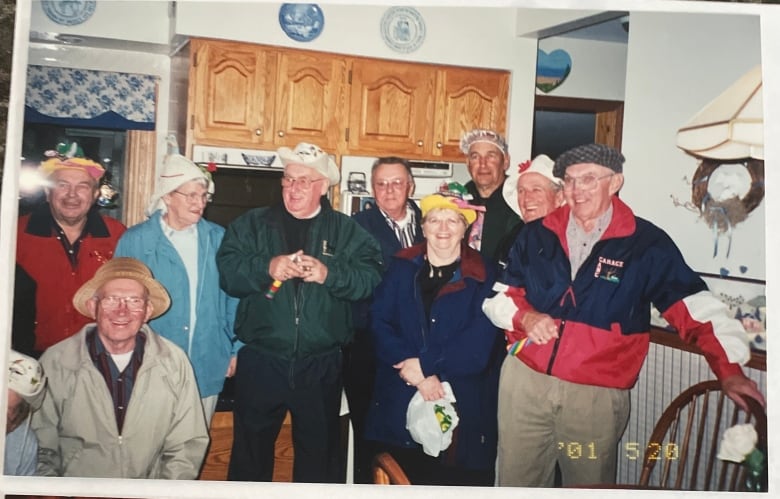 A vintage photo of a group of people standing in a 1980s-era kitchen wearing jackets and bizarre hats.