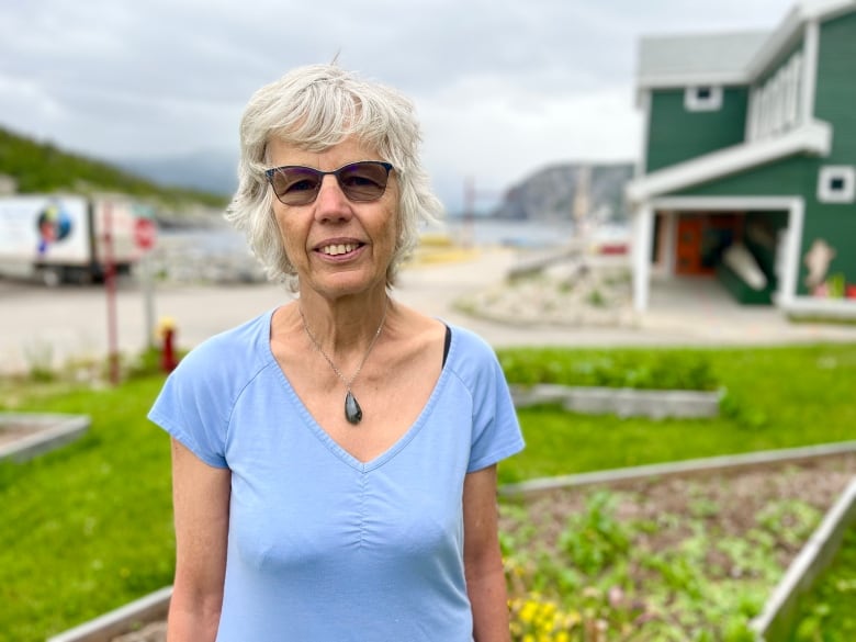A woman smiles for the camera against a backdrop of a garden and harbour.