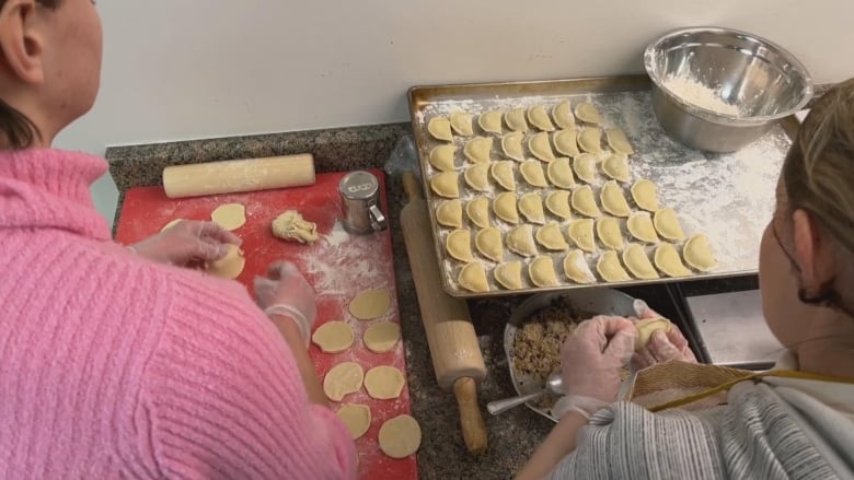 Two women stuff pierogi dough in a kitchen.
