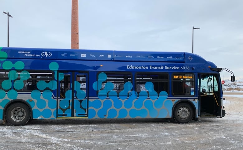 A large blue bus with its front door open sits in a parking lot.