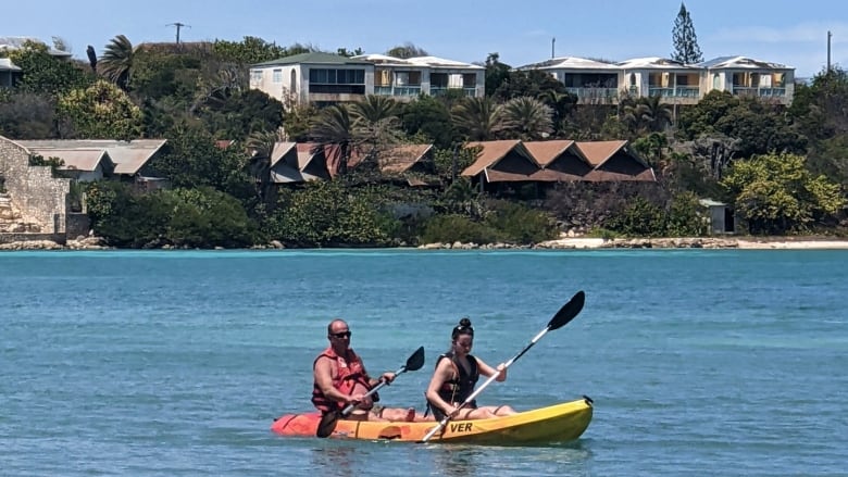 A man and younger woman paddle a kayak in a tropical setting.