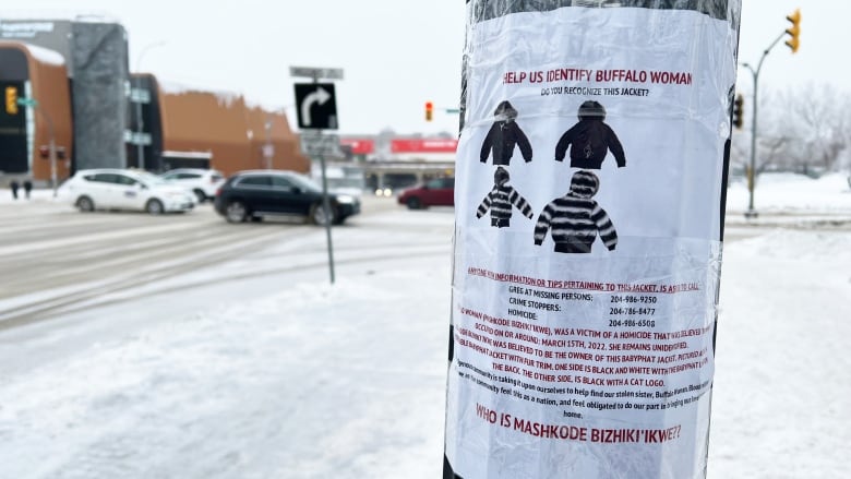 A poster with red and black text is taped to a light pole on Main Street. A snowy sidewalk is visible in the background. 