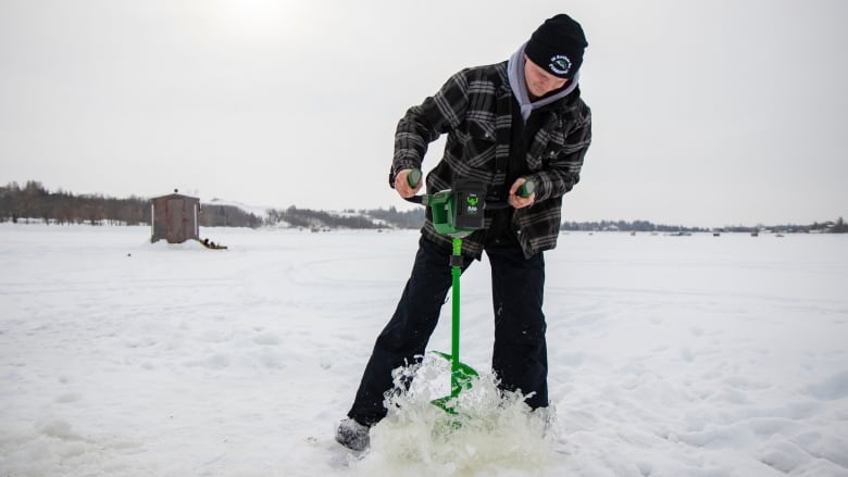 A young man uses an electric auger to drill a hole for ice fishing.