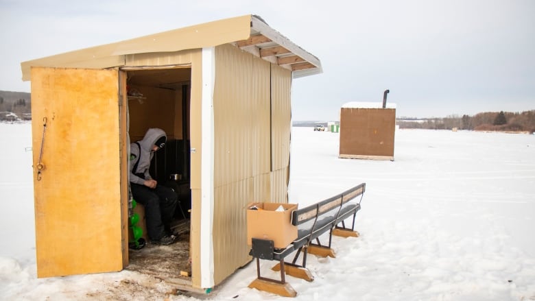 A man sits in an ice fishing shack.