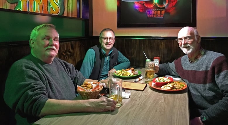 Three men sit around a restaurant table with food and drinks.