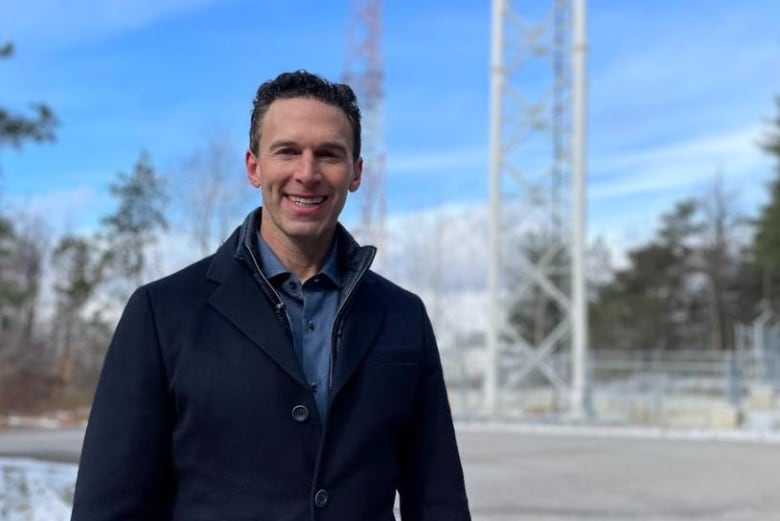 The founder of Wind Mobile is standing in front of two cellphone towers on a chilly day.