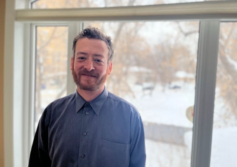 A man smiles in front of a window in the winter. 