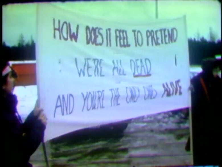 Protesters hold a sign that reads: How does it feel to pretend we're all dead and you're the only ones alive.
