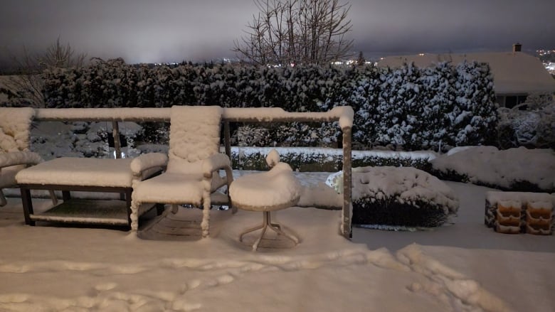 Heavy snow covers a patio and outdoor furniture in dim, early morning light. 
