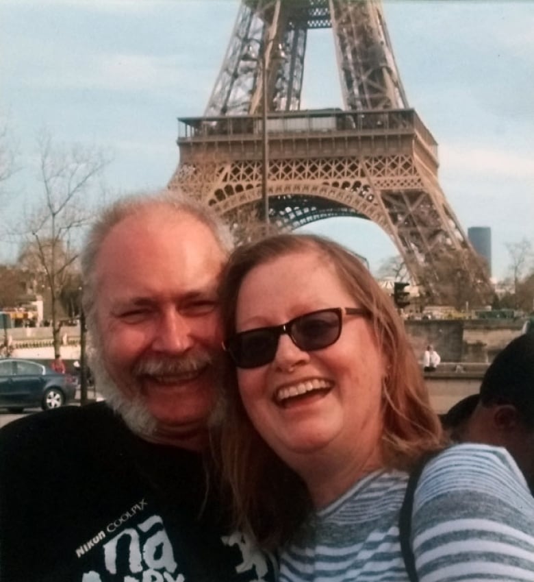 A man and woman smile in front of the Eiffel Tower.