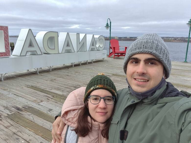A smiling man and woman pose for a selfie at a harbourfront. 