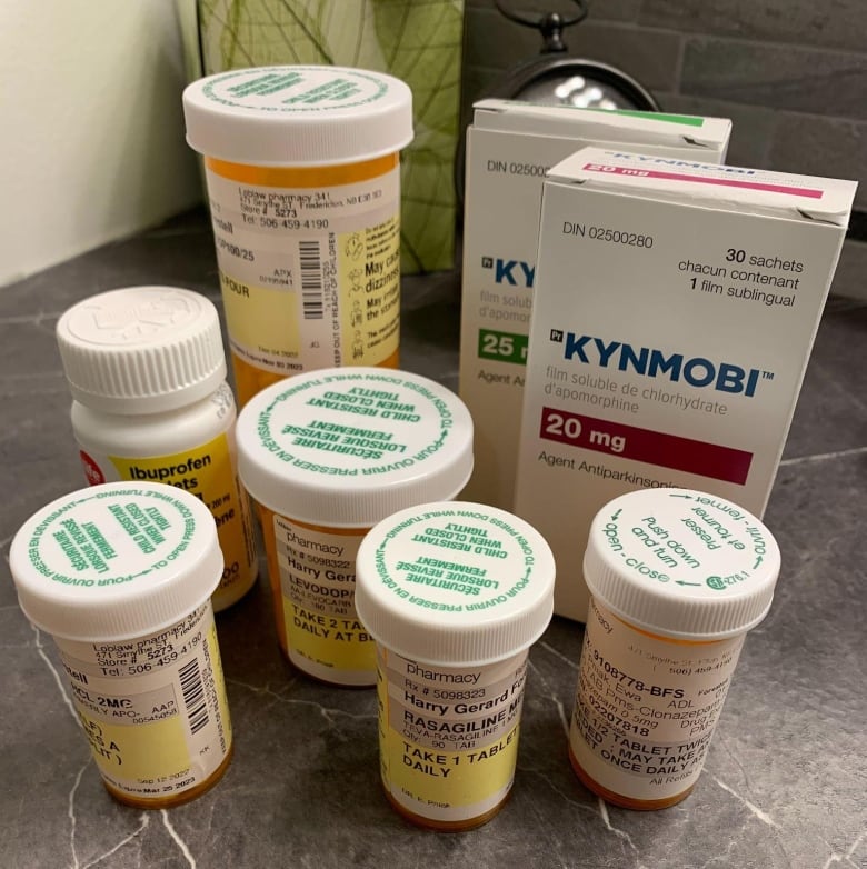 Five small bottles of medications sit on a bathroom counter, with a larger bottle and two boxes behind them. 