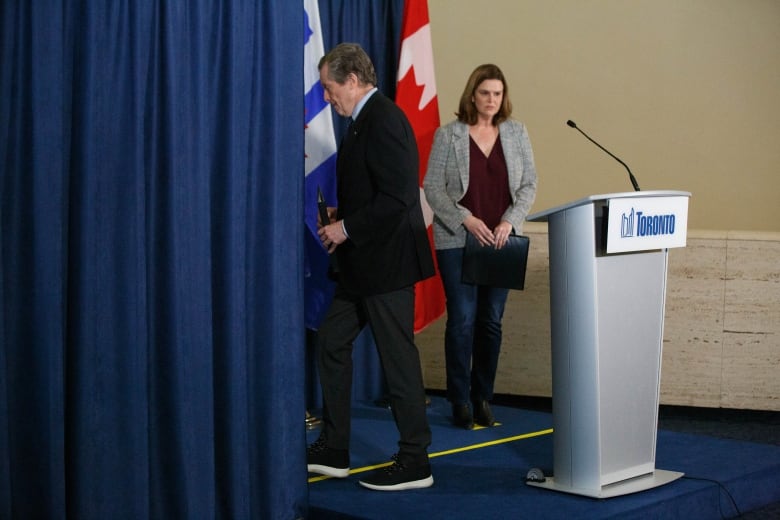 A woman gets ready to speak at a podium as a man walks away from the podium. 