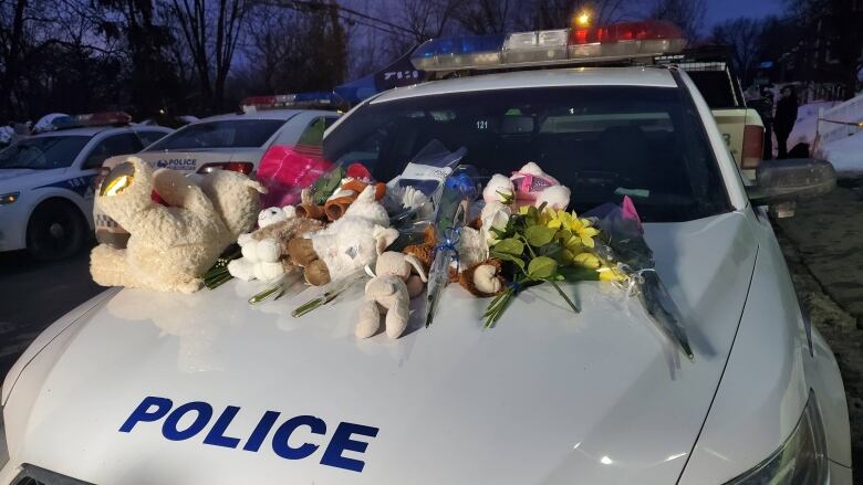 A police car covered in stuffed animals and flowers. 