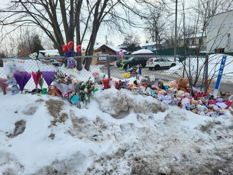 Stuffed animals, flowers and cards sit atop a snowbank outside a daycare. 