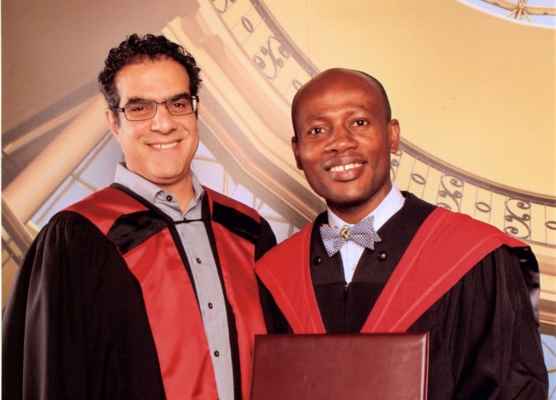 Two men in black and red robes grin for the camera. One is holding a certificate. 