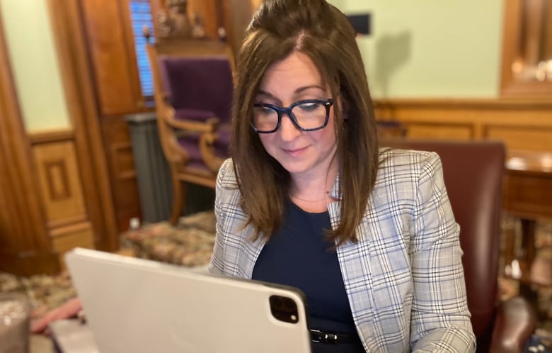 A woman sits at a table in front of a laptop computer in the new Brunswick legislature.