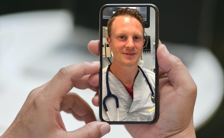 A man is seen in scrubs on a phone.