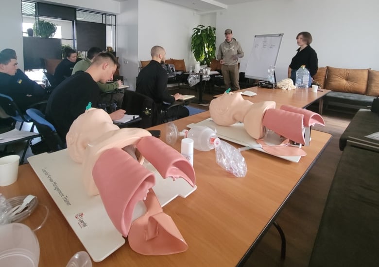 Mannequins can be seen on a table in front of participants of the combat first aid training.