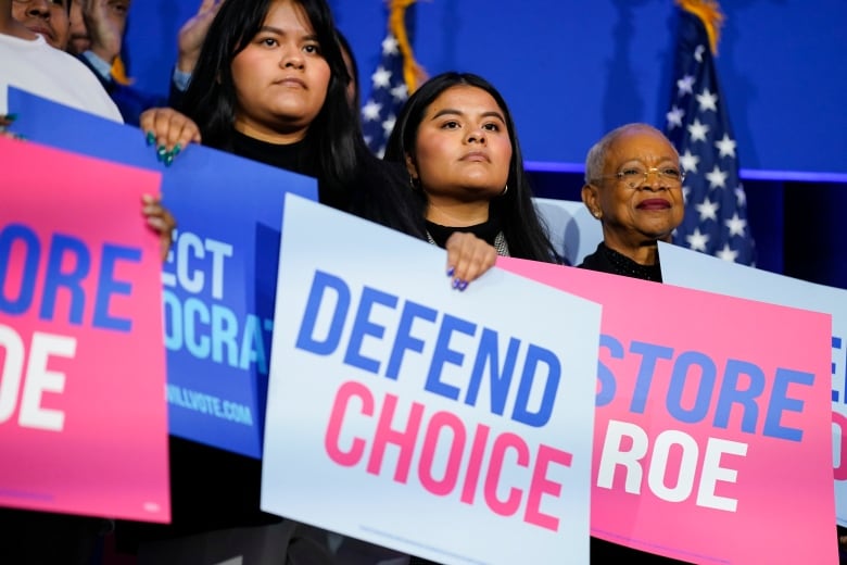 Individuals standing listening to a speech, holding signs that read 'Defend Choice.'