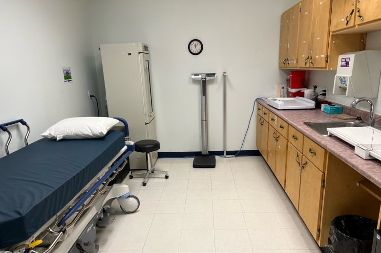 A small room with medical equipment, including a patient bed, a sink, wooden cupboards and a weigh scale.