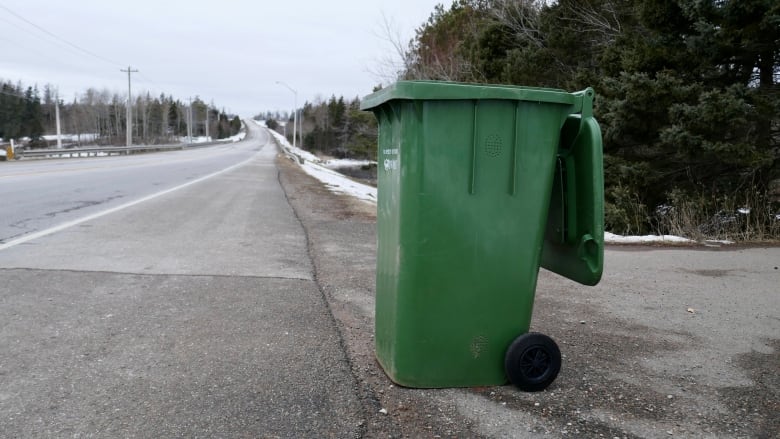 A green bin with the lid open sits by the side of a highway. 