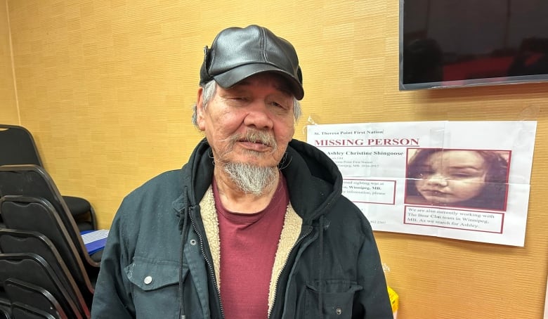 A man with a leather cap, red t-shirt and black winter jacket is pictured in a hotel room in front of a missing persons poster.