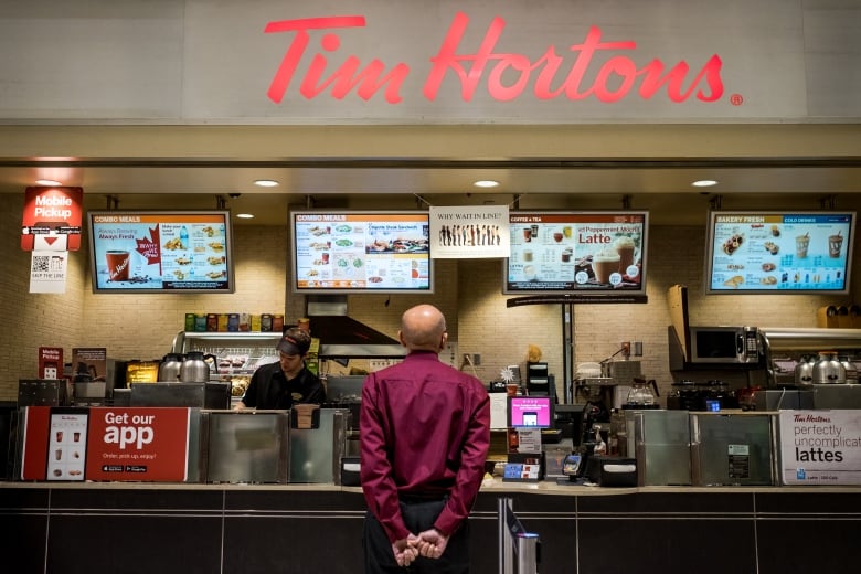 A customer at a Tim Hortons reads the menu while a worker makes a drink behind the counter.