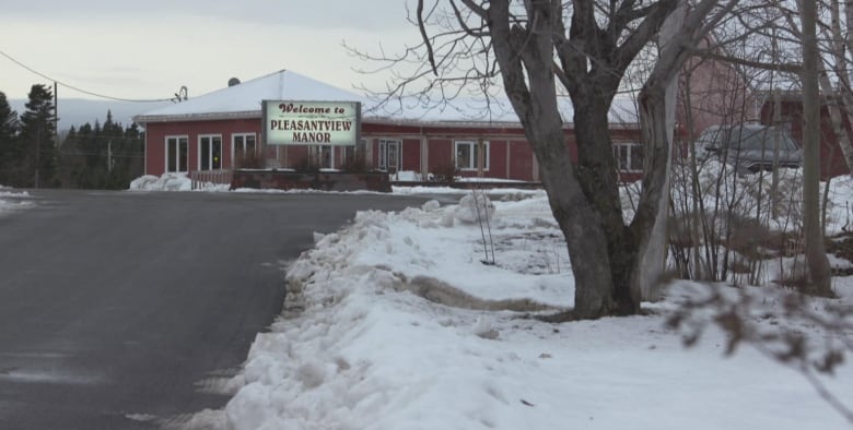 A single-storey building is shown at the end of a long driveway, with snow covering the ground and the building's roof. An illuminated sign out front reads: Welcome to Pleasantview Manor.