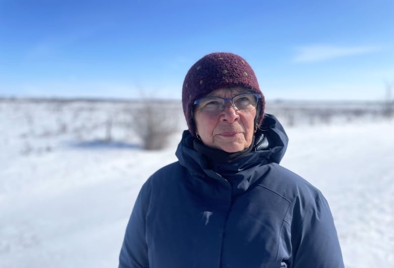 A woman stands in a frozen field, wearing a tuque.